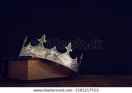 low key image of beautiful queen/king crown over old book and wooden table. vintage filtered. fantasy medieval period Royalty-Free Stock Photo #1585217923