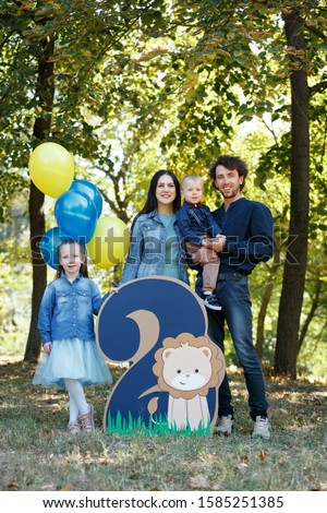 Family life. Portrait of parents and their children in the Park. Birthday of a two year old boy. Decor with the number two with lion and balloons. Vertically framed shot.