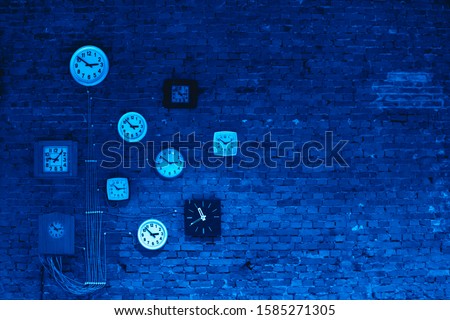 Collection of vintage wall clocks hanging on an old brick wall in blue colors. Color of the 2020 year.