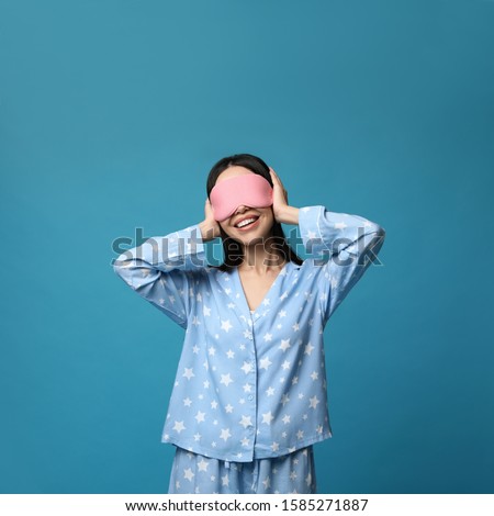 Young woman wearing pajamas and sleeping mask on blue background. Bedtime Royalty-Free Stock Photo #1585271887