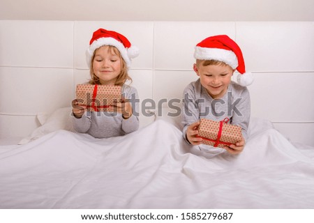 Amazed children open gifts on Christmas morning. Happy school boy and girl in white bed