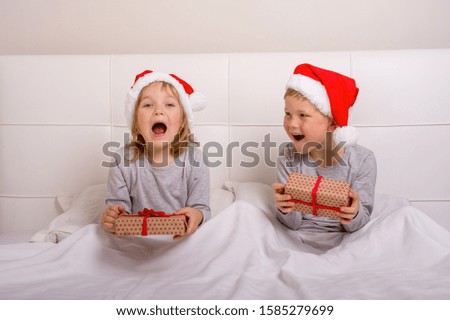 Amazed children open gifts on Christmas morning. Happy school boy and girl in white bed