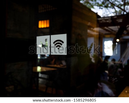 Signs on glass door. No smoking sign, wireless signal icon sign for free wifi on cafe background. Decal sticker signs pasted on front door outside the coffee shop.