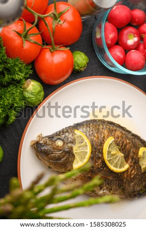Tasty fish cooked with lemons on a background of fresh vegetables.Vertical frame