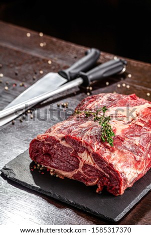 Raw meat. Beef tenderloin, neck lies on a black board, next to a knife and knife sharpener. closeup. background image. copy space