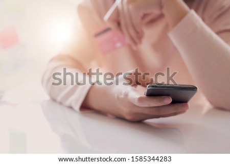 Close up hand of woman holding credit card and using smart phone at home. Online shopping concept.