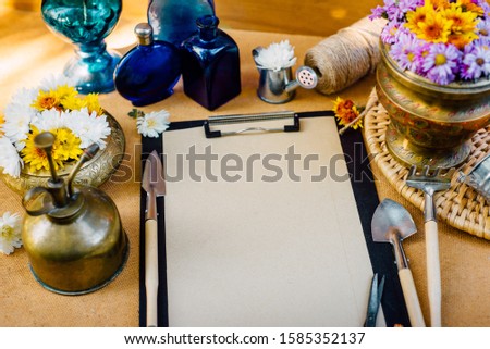 Vintage composition. Closeup clip board with scissors and vintage garden tools with flowers around on wooden background. Top view