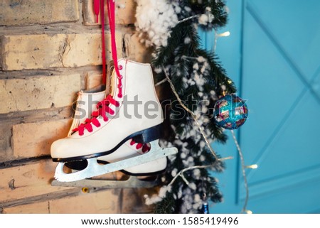 Pair of white vintage leather skates with red laces hanging on old rustic brick wall with garland lights on christmas tree decoration. Cozy scenic christmas card interior winter holidays background
