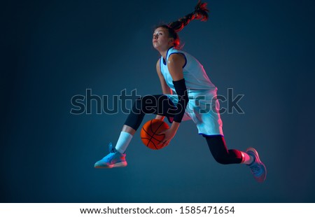 Flight. Young caucasian female basketball player on blue studio background in neon light, motion and action. Concept of sport, movement, energy and dynamic, healthy lifestyle. Training, practicing.