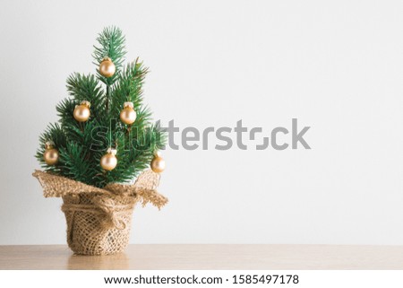 Simple small Christmas tree with golden yellow baubles on wooden floor. Closeup. Empty place for positive text, inspirational quote or sayings on gray wall.