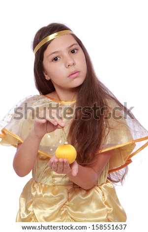 Studio portrait of a beautiful smiling young girl with long dark hair in a gold fancy dress holding a yellow Christmas ball on a white background