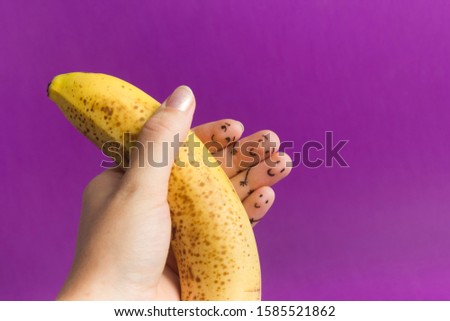 Painted funny fingers smiley holding yellow banana against purple background