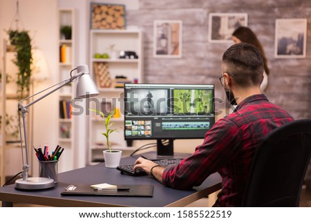 Back view of creative filmmaker working on a movie on laptop. Girlfriend in the background. Royalty-Free Stock Photo #1585522519