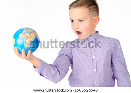 Playful young caucasian school boy holding a globe on white studio background.Boy is surprised.