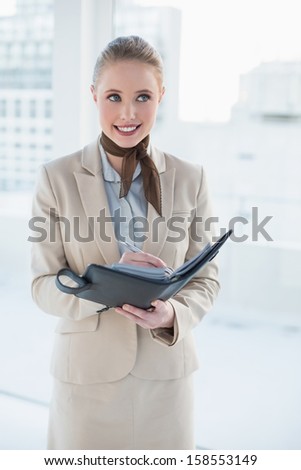 Blonde smiling businesswoman holding a diary in bright office