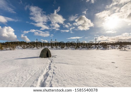 Camouflage tent on a snow covered bog with cloudy sky