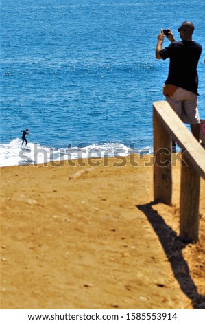 A vertical shot of a male taking a picture of a surfer enjoying the day perfect for practicing his sport in the ocean