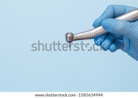Dentist's hand in a latex glove with high-speed dental handpiece on blue background. Medical tools concept. Royalty-Free Stock Photo #1585634944
