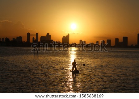 The woman is paddling in the sunset in Miami.