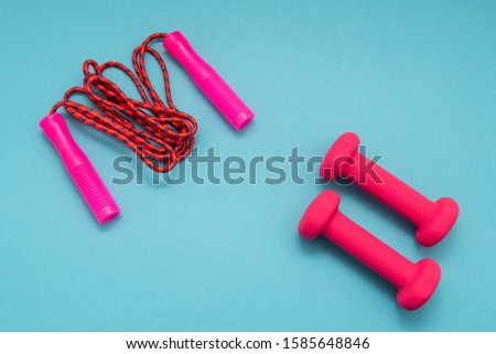 Pink dumbbells and jump rope on blue background.Sports, fitness and healthy lifestyle concept.