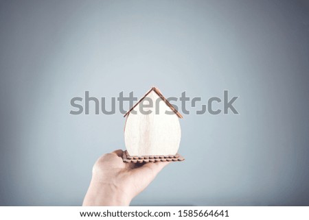 woman hand holding wooden house model on gray background