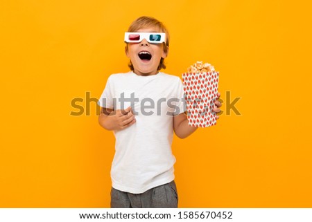 boy in glasses for a movie theater with popcorn watching a movie in surprise on a yellow background