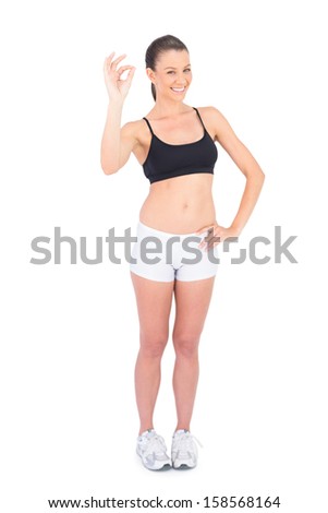 Portrait of happy woman in sportswear making okay gesture on white background