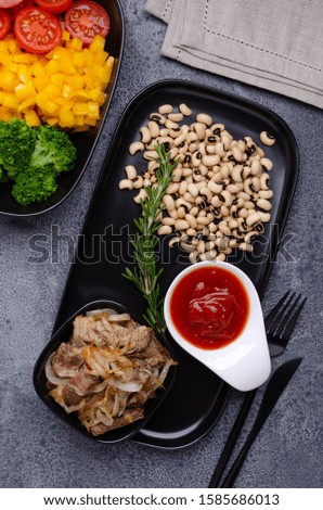 Beans with vegetables and meat in a black dish on a slate background.  Selective focus.