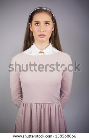 Serious pretty model with pink dress on looking up on grey background