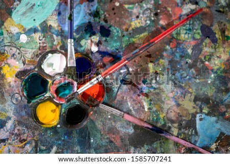 Top view, set of old art materials,palette with watercolor,artistic brushes,color palette and paintbrushes for painting on the table that gets the paint stain background, creative,development concept