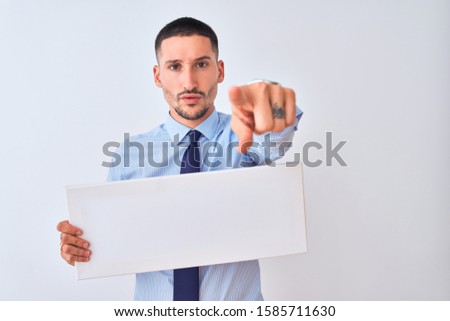 Young business man holding blank banner over isolated background pointing with finger to the camera and to you, hand sign, positive and confident gesture from the front