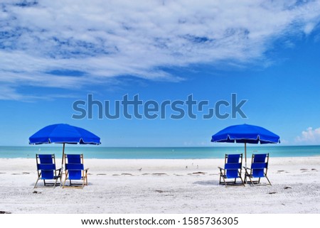 Brilliant blue umbrellas against white clouds and blue sky on the beach of Caladesi Island in Dunedin, Florida.  Sand and seagrass, no people.