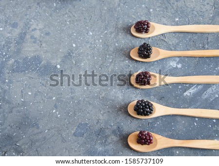 Summer berry Blackberry lies in a wooden spoon on a gray concrete background. Six wooden spoons lie parallel to each other. Background, pattern, horizontal, soft focus