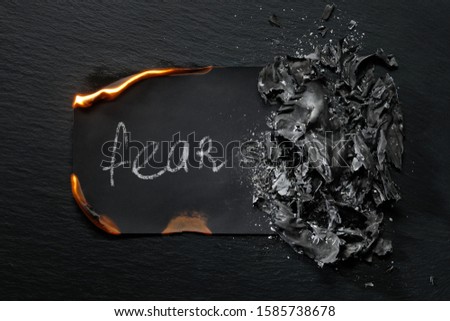 Burning piece of black paper with the word "FEAR "on a black background.