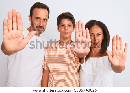 Family of three, mother, father and son standing over white isolated background doing stop sing with palm of the hand. Warning expression with negative and serious gesture on the face.