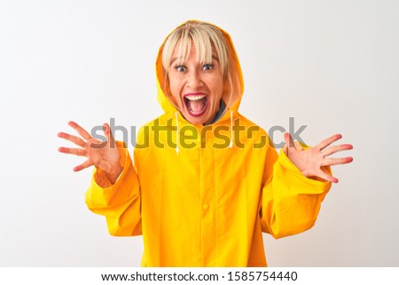 Middle age woman wearing rain coat with hood standing over isolated white background celebrating crazy and amazed for success with arms raised and open eyes screaming excited. Winner concept