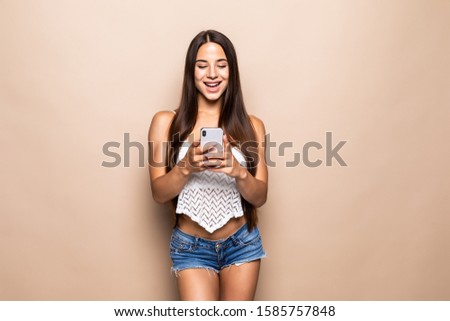 Young woman typing on the phone over beige background