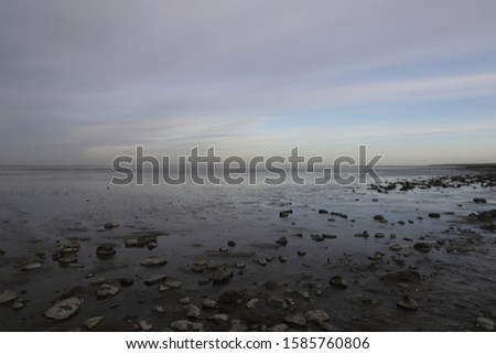 Panoramic view of the Dutch Wadden Sea with a beautiful sky, photo was taken in December.  There's a selective focus on the stones creating a panoramic view over the sea and sky.