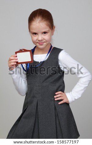 Image of lovely little girl in a school uniform with a name tag on a gray background/Little girl with a blank name tag