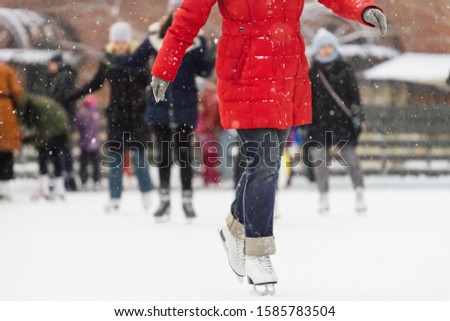 Girl in red jacket and in white old fashion skates riding on an outdoor ice rink. Snow is falling. Winter leisure and recreation. Selective focus, blurred background, close up photo. Seasonal concept.