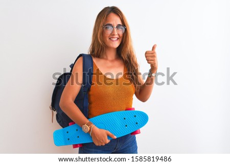 Young redhead student woman wearing backpack and skateboard over isolated background happy with big smile doing ok sign, thumb up with fingers, excellent sign