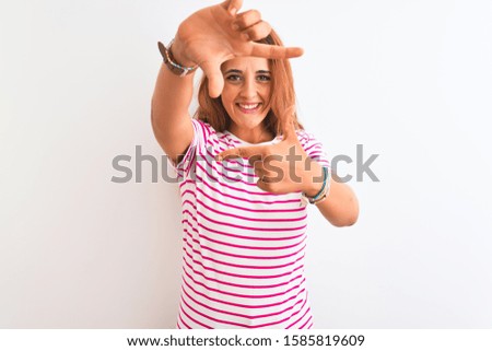 Young redhead woman wearing striped casual t-shirt stading over white isolated background smiling making frame with hands and fingers with happy face. Creativity and photography concept.