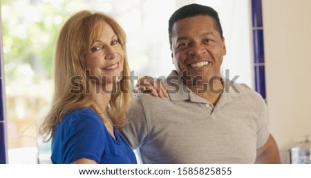 Happy Senior mixed race couple homeowners looking at camera. Older Caucasian and African American husband and wife standing in their kitchen smiling Royalty-Free Stock Photo #1585825855