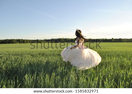 The bride is spinning in her wedding dress. Bride in the field. The sun's rays illuminate the bride. The bride's shadow falls on the green field. Forest in the background.