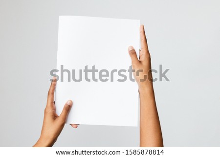 Black, Southeast Asian or ethnic model holding a blank mock-up or dummy of an A5 or half letter-sized brochure or report with both hands. Studio shot on white.