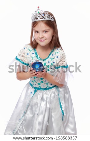 Studio image of emotional lovely little girl in a beautiful dress and a crown holding a Christmas decoration