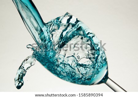 Blue food coloured water splashing in a wineglas Royalty-Free Stock Photo #1585890394