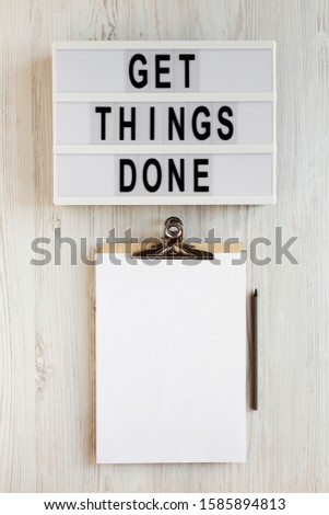 'Get things done' words on a modern board, clipboard with blank sheet of paper on a white wooden surface, top view. Overhead, from above, flat lay. 