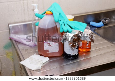 Unlabeled chemicals with gloves resting on top on a steel counter top next to a sink Royalty-Free Stock Photo #1585901389