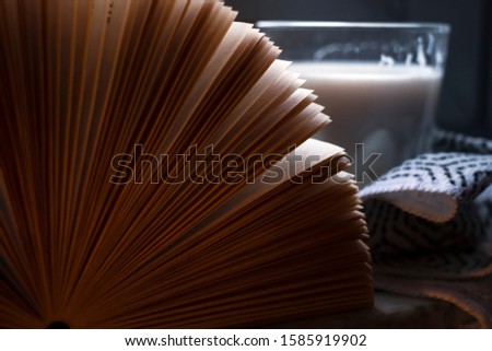 Open book near the window on a rainy day, with glass of hot milk in the background